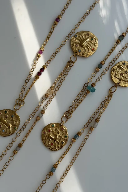 Kolekcja złocistych naszyjników zodiakalnych Lulobelia. W górnej części zdjęcia widoczny jest medalion Skorpiona, a obok naszyjniki innych znaków.